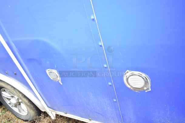 Blue exterior of a commercial mobile kitchen trailer, showing ventilation ports and tire. Wear visible on surface.