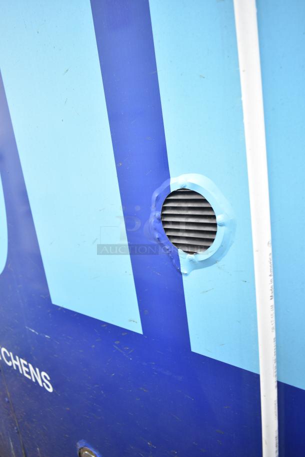 Blue and white exterior of a commercial mobile kitchen trailer with vent detail, showing signs of wear.