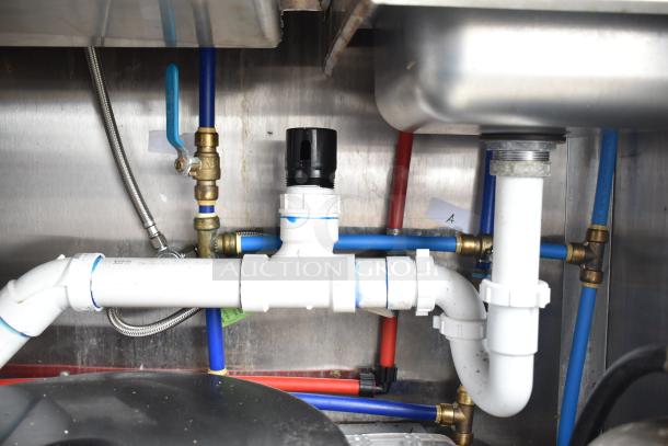Plumbing connections under sink in a commercial mobile kitchen trailer, showing pipes and fittings.