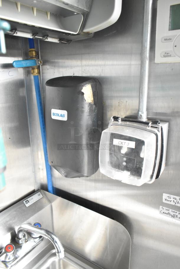 Interior of a commercial mobile kitchen trailer featuring an Ecolab dispenser, control panel labeled "CKT 3," and a stainless steel sink with dual faucets.
