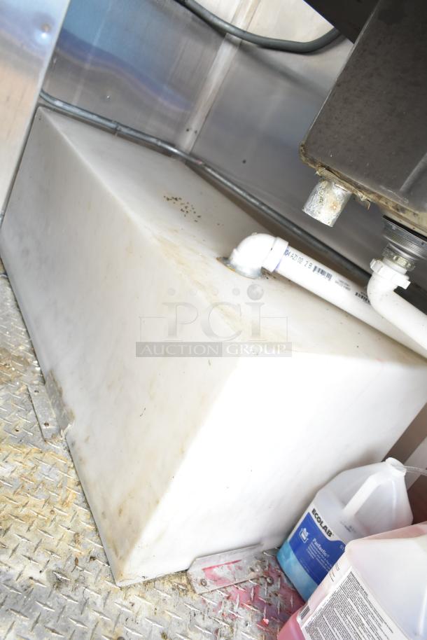 Mobile kitchen trailer interior showing a large white water tank, PVC plumbing, and cleaning supplies stored nearby.