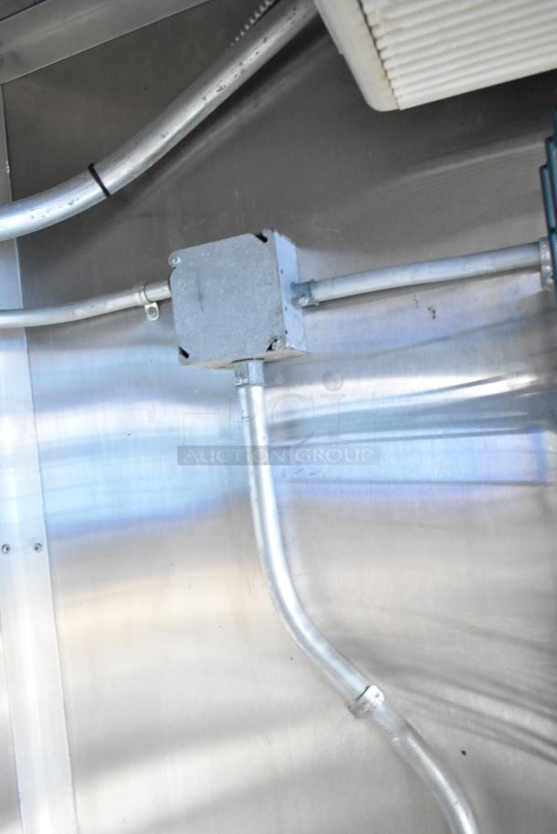 Interior view of mobile kitchen trailer showing metal conduit and pipework against stainless steel wall.