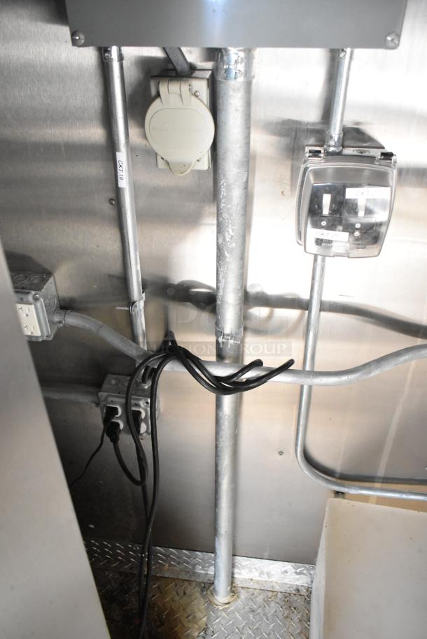 Electrical setup of commercial mobile kitchen trailer, featuring wiring and outlets on metal wall with industrial piping.