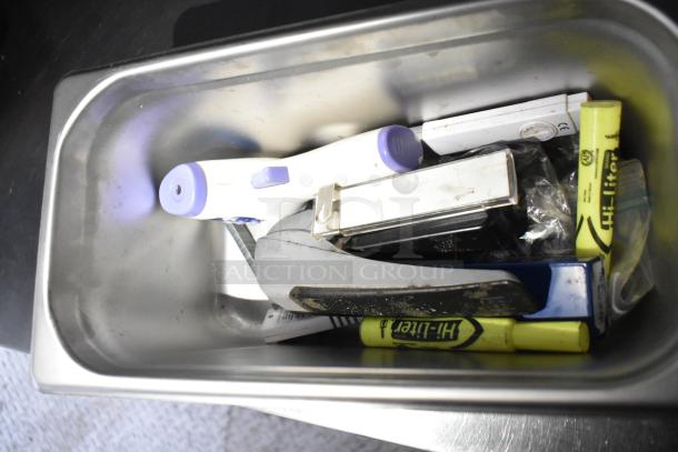 A stainless steel container filled with various office supplies, including highlighters, a stapler, and a tape dispenser.