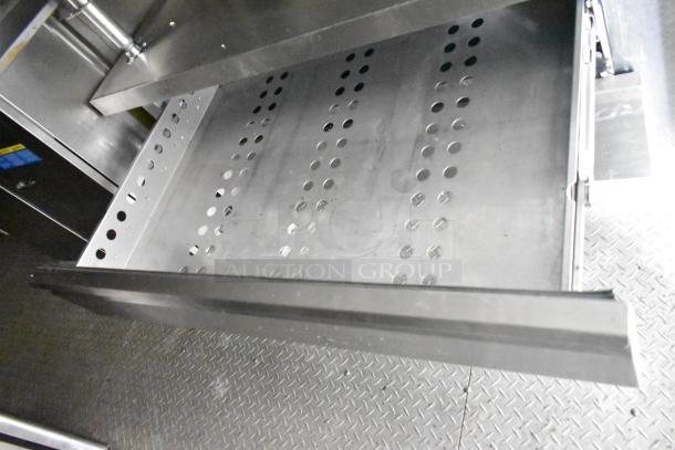 Open stainless steel drawer in commercial mobile kitchen trailer, showing perforated metal surface for ventilation.