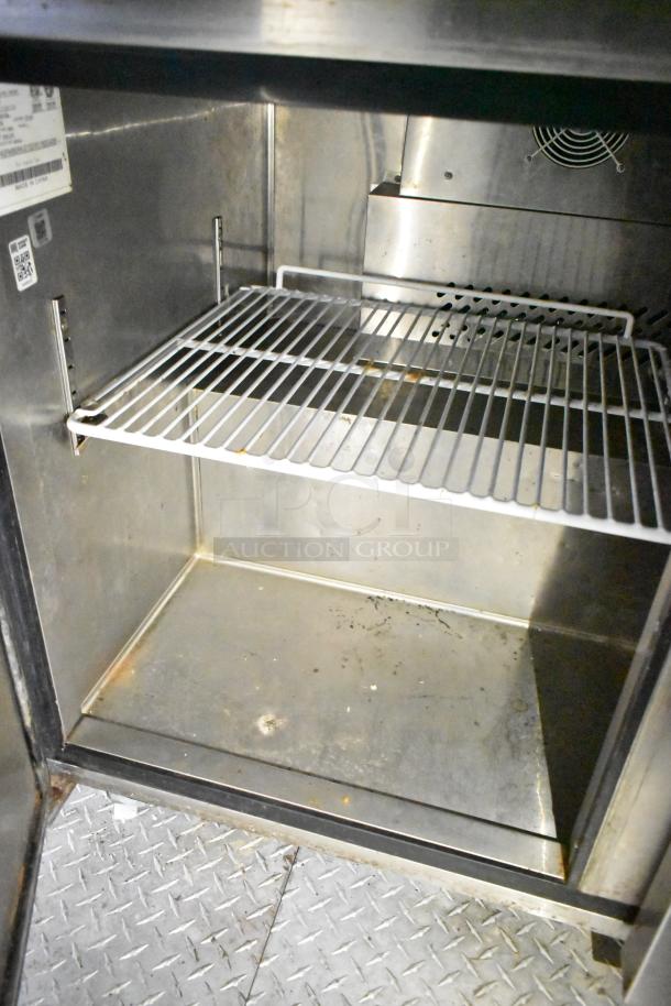 Interior of a stainless steel commercial mobile kitchen trailer, showing shelving and diamond plate flooring.