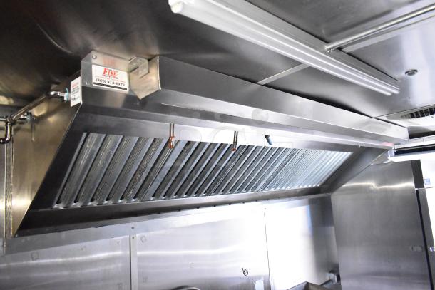 Mobile kitchen trailer interior with CaptiveAire hood system, stainless steel finish, and mounted fire protection tag.