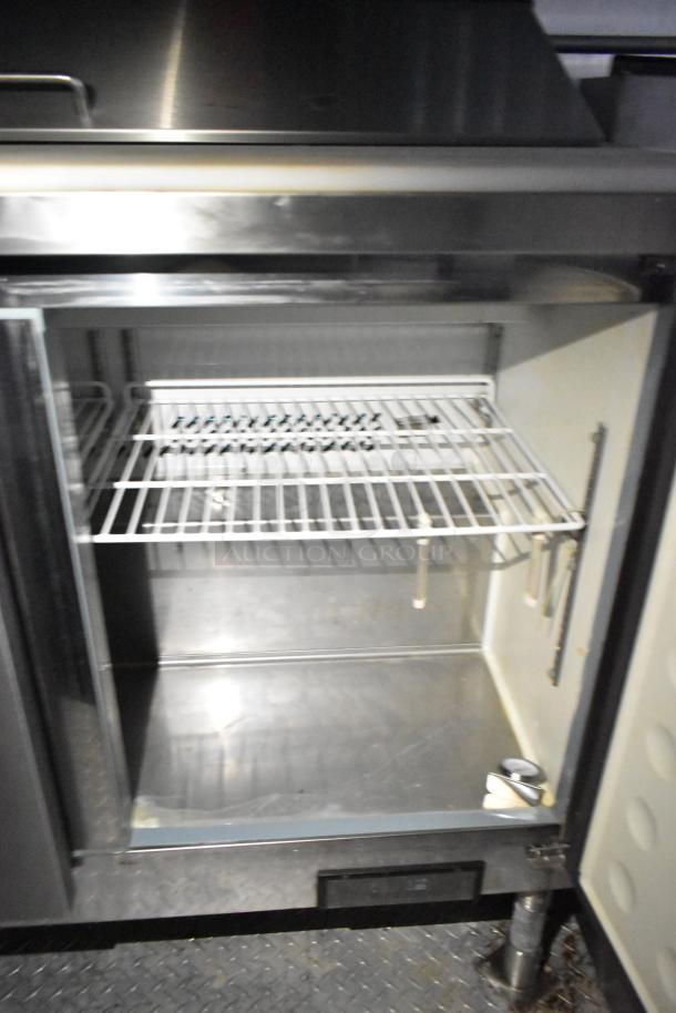 Stainless steel refrigeration unit inside commercial mobile kitchen trailer, featuring wire shelving and secure latch.