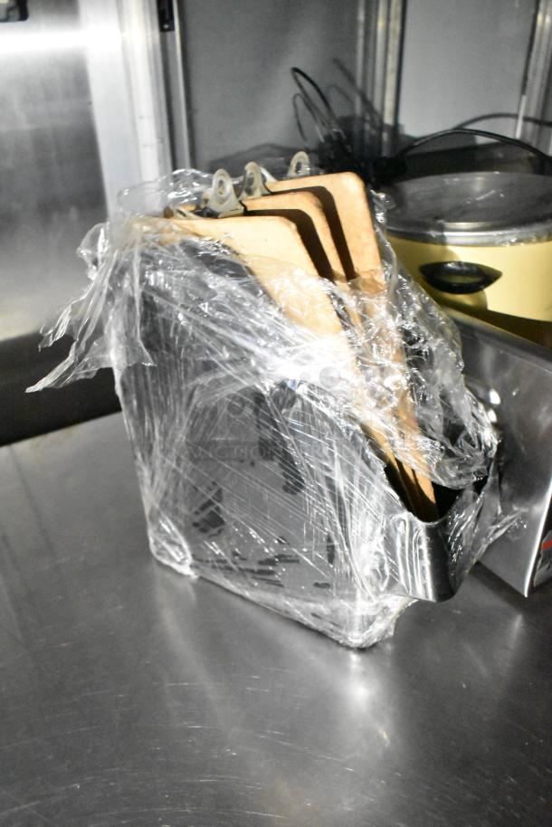 Wrapped items on a stainless steel surface inside a commercial kitchen trailer. Plastic wrap covers three wooden boards.