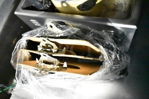 Plastic-wrapped metal clasps on a shelf, possibly part of a commercial kitchen trailer's equipment.
