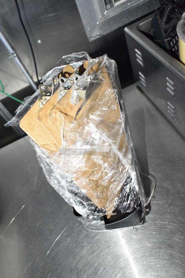 Clear plastic-wrapped set of clipboards on a metal surface inside a mobile kitchen.
