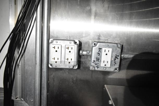 Electrical outlets inside a commercial mobile kitchen trailer, set against a metal wall, with visible wiring and handwritten labels.
