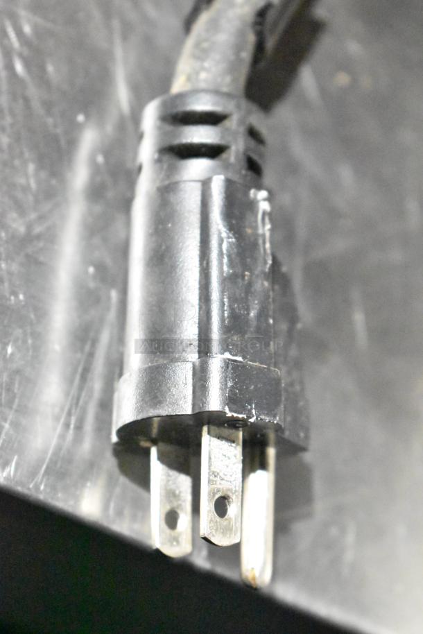 Electrical plug with three prongs connected to a black cable, likely part of commercial kitchen equipment.