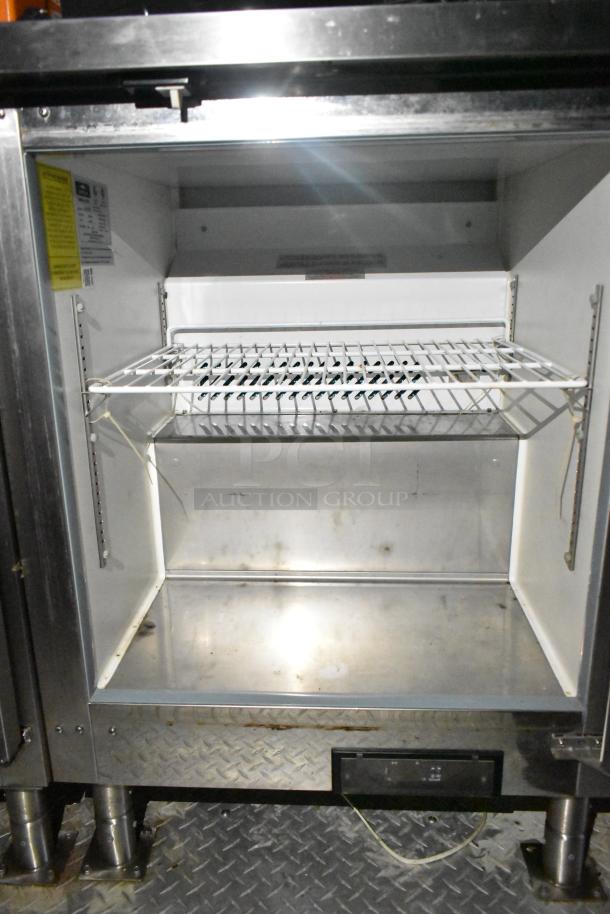 Interior of a commercial mobile kitchen trailer. Features a clean, metal refrigeration unit with shelving and adjustable rack.