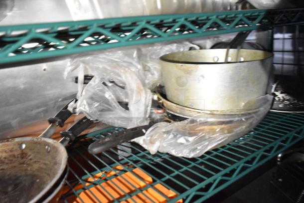 Metal pots and frying pans on green shelving inside a commercial mobile kitchen trailer. Handles are wrapped in plastic.
