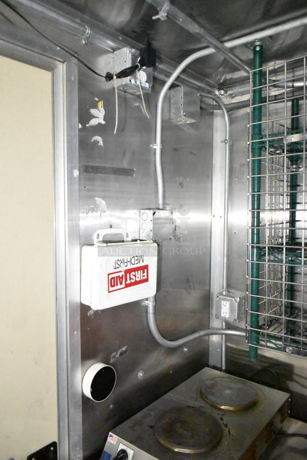 Commercial mobile kitchen trailer interior, featuring stainless steel wall, first aid kit, electrical outlets, and metal shelving.