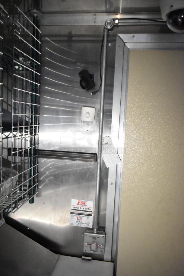 Commercial mobile kitchen trailer interior, featuring metal walls, a fire protection tag, and grid shelving system.