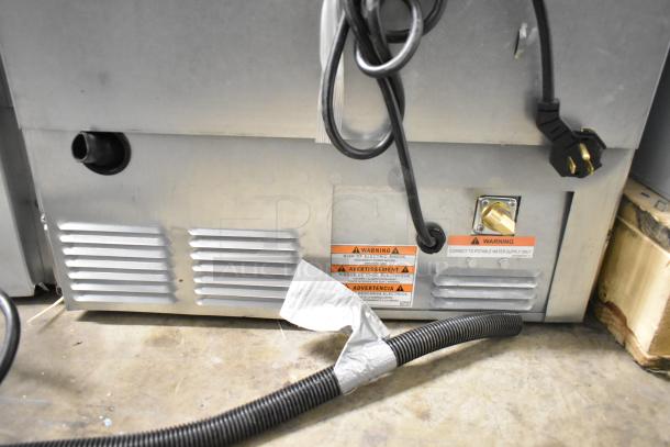 Brand new Manitowoc UDP0065A-161 commercial ice machine, 115V, showing back panel with cables and warning labels.