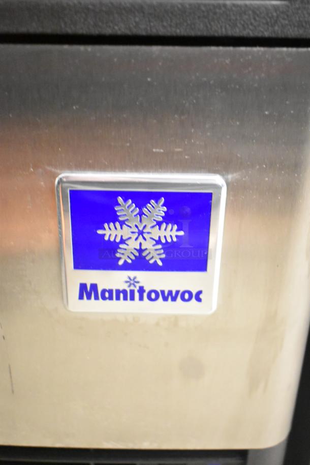 Manitowoc brand logo on stainless steel panel of UDP0065A-161 ice machine, showing minor scratches and dents.