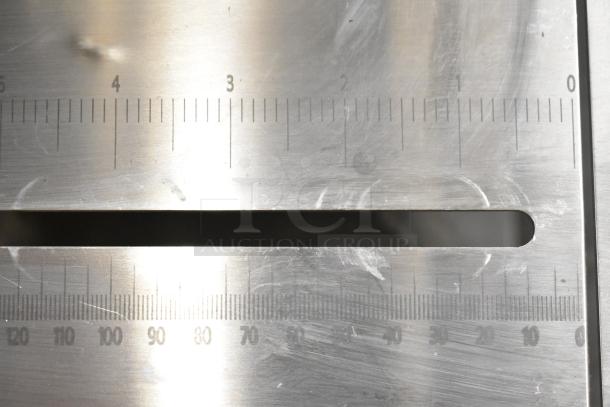 Close-up of Backyard Pro 554BSSW65AL Band Meat Saw table surface with measurement markings. New condition, slight scratches visible.