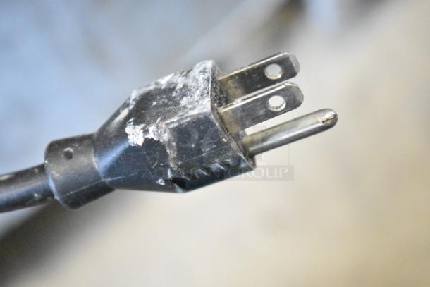 A close-up of a worn electrical plug with visible dust and minor scratches on the prongs and casing.