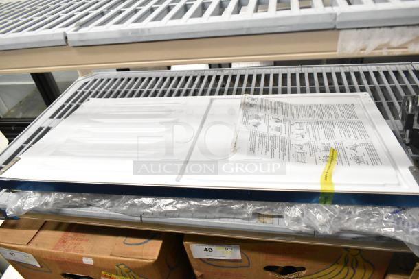 Brand new Hoshizaki ice maker door with minor scratches, in original packaging on a metal shelf. Assembly instructions visible.