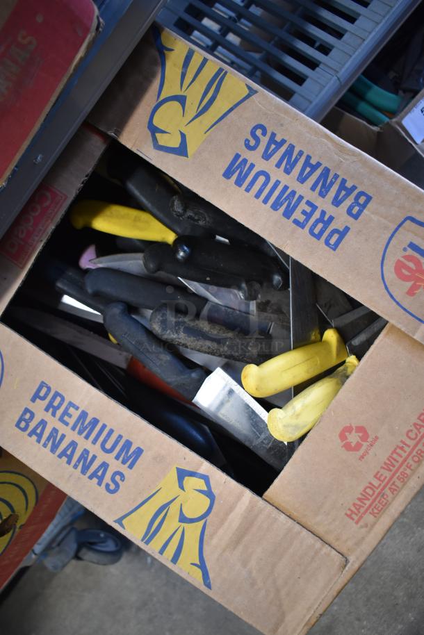 Cardboard box containing 100 assorted sharpened stainless steel knives, including chef knives, with various colored handles.