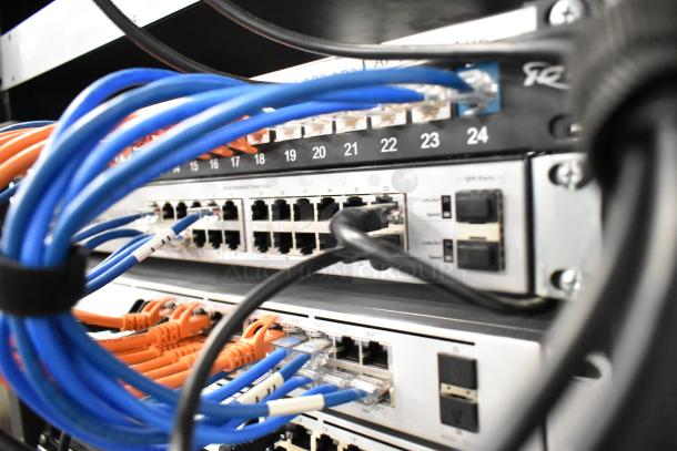 AV cabinet with network and audio equipment connected. Includes switches, amplifiers, a modem, controllers, and various cables.