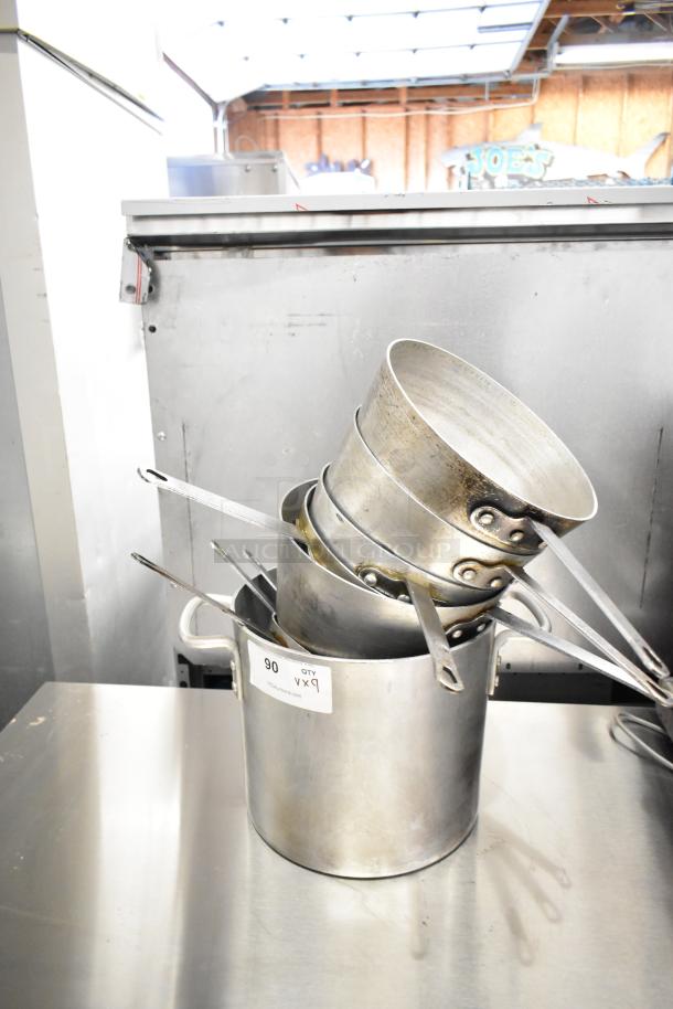 Nine metal sauce pots and stock pot set displayed. Visible auction label "90 QTY 9X". Used condition.