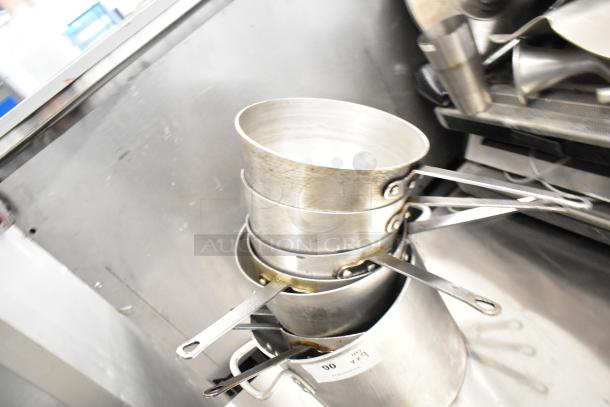 Aluminum sauce pots and stock pot stack, metal handles, some wear. Auction label visible. Lot of 9 items.