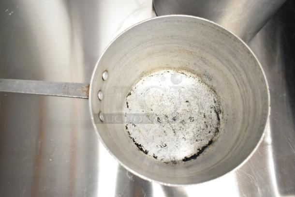 Metallic sauce pot with visible wear, including scratches and residue, on a reflective surface. Part of a 9-item cookware set.