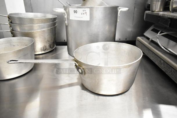 Nine aluminum kitchen pots, including sauce pots and a stock pot, used condition, stacked on a metal surface. Quantity label: 9x.