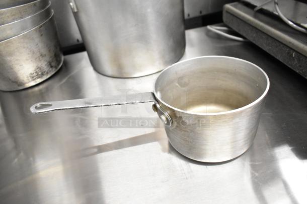 9 various kitchen items including sauce pots and stock pot on a metal surface, showing used condition.