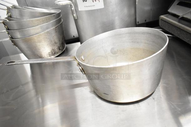 Nine metal sauce pots and a stock pot, used condition, stacked on a stainless steel surface, auction lot label visible.
