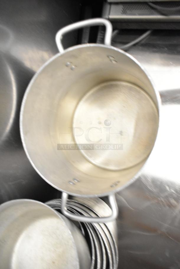 Nine metal cooking pots, including sauce pots and stock pot, stacked together. Visible handles and slightly used condition.