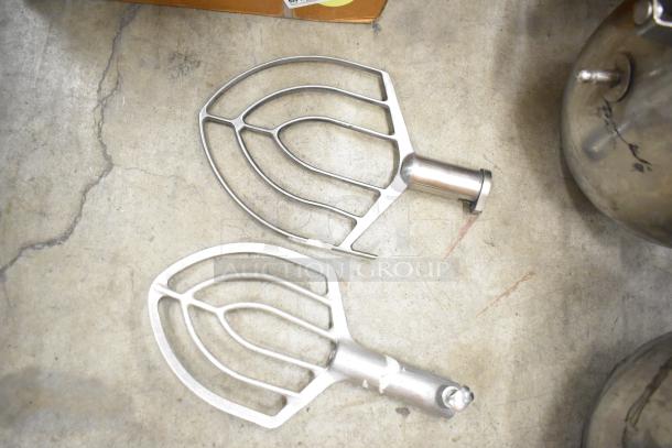 Two paddle attachments for Hobart mixer, metal construction, shown on concrete surface, with mixing bowls partially visible.
