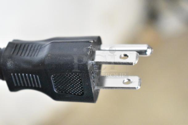 Close-up of a standard three-prong electrical plug connected to an appliance, showing minor scratches on the plastic body.