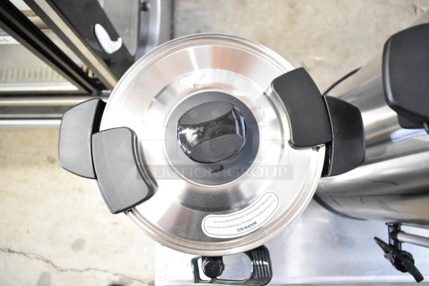 Stainless steel coffee urn with black handles and warning label. Part of a new, scratch and dent auction lot.