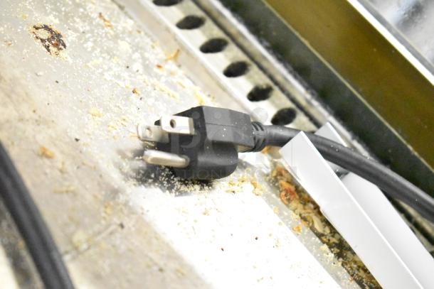 Vollrath HDE8460 Heated Display Case plug, showing three-prong design against crumb-covered surface. 120 Volts, 1 Phase.