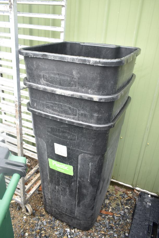 Three black Rubbermaid trash cans stacked and one green poly trash can, showing wear, labels indicate use for plastics.