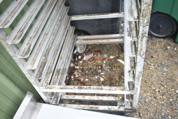 Metal commercial pan transport rack with visible wear and rust, featuring multiple slots and commercial casters.