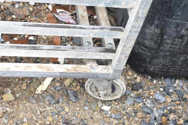Metal commercial pan transport rack with visible signs of wear, mounted on durable commercial casters.