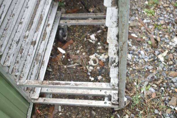 Commercial pan transport rack on caster wheels, showing signs of wear and rust, suitable for industrial use.