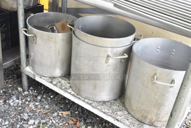 Commercial table with four large stainless steel stock pots in used condition, placed on a sturdy metal shelf.
