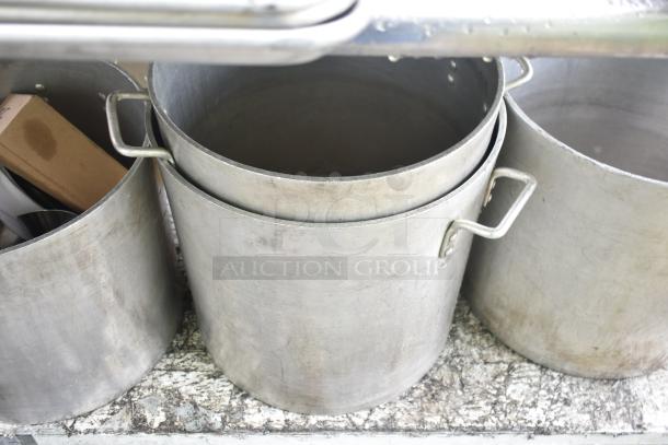 Commercial table with four large metal stock pots, showing minor wear, suitable for industrial use.