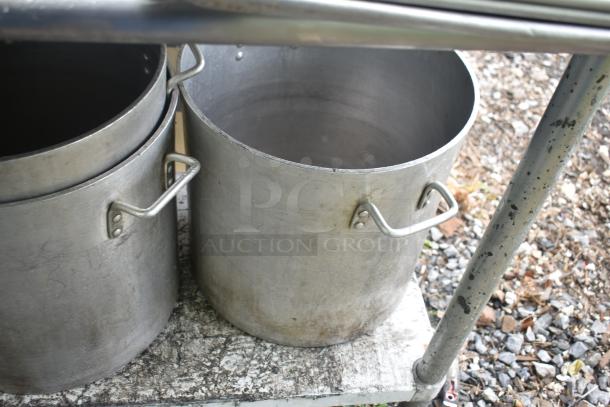 Commercial table with four large metal stock pots, weathered condition, featuring sturdy handles and visible wear.