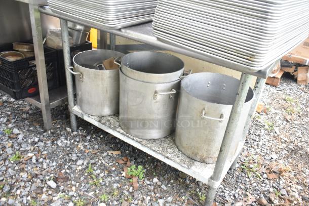 Commercial metal table with four large stock pots underneath, showing signs of wear, ideal for kitchen use.