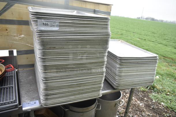 104 metal full-size baking pans stacked, showing light wear, marked with auction details indicating 4/19 QTY x 104.