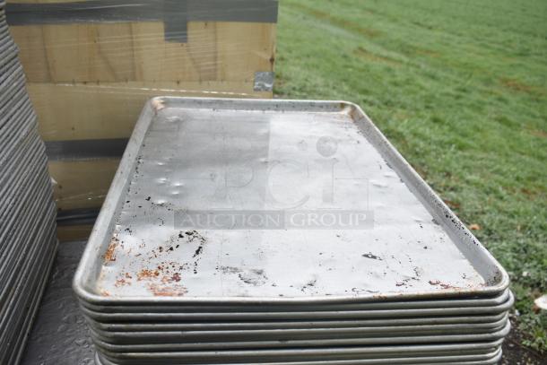 104 full-size metal baking pans, slightly worn with visible surface rust and dents, stacked outdoors.