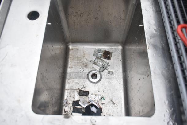 Stainless steel single bay sink with various kitchen contents inside, showing signs of use and wear.